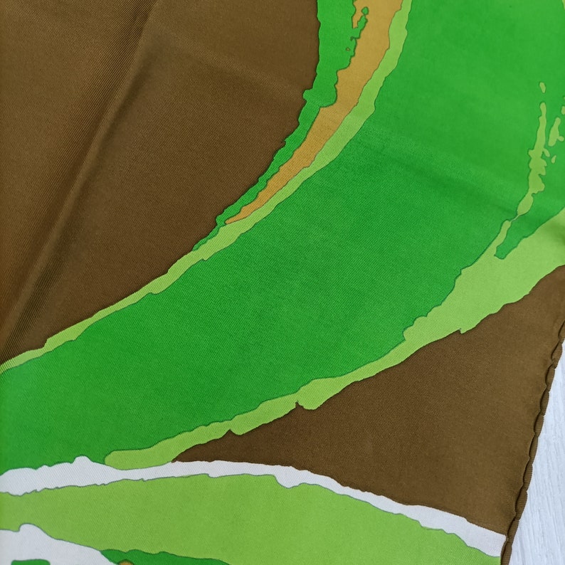 Op de afbeelding: Een bruine zijden sjaal met een abstract ontwerp in groen, wit en geel.