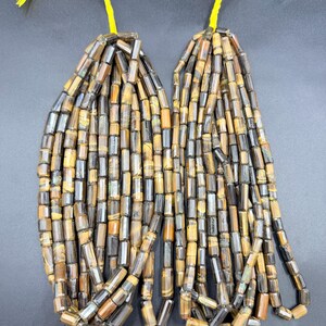 May include: Two strands of rectangular tiger eye beads, each with a yellow string. The beads are a mix of brown, black, and gold colours. The beads are approximately 0.6 cm in length.