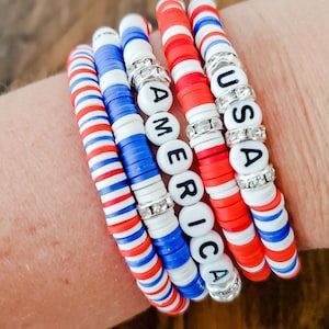 May include: Four bracelets with red, white, and blue beads. The bracelets spell out "USA" and "AMERICA" in black letters.