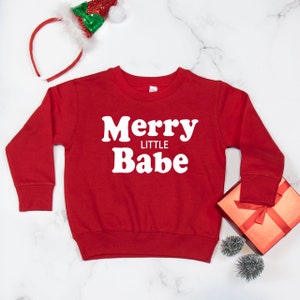 May include: Red Christmas sweatshirt with white text that reads "Merry Little Babe".