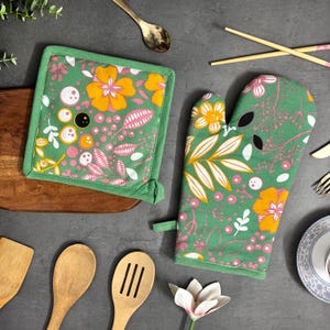May include: A green and floral oven mitt and matching square pot holder. The set features a vibrant pattern of orange and pink flowers, white leaves, and black accents. The pot holder is square with a green border.