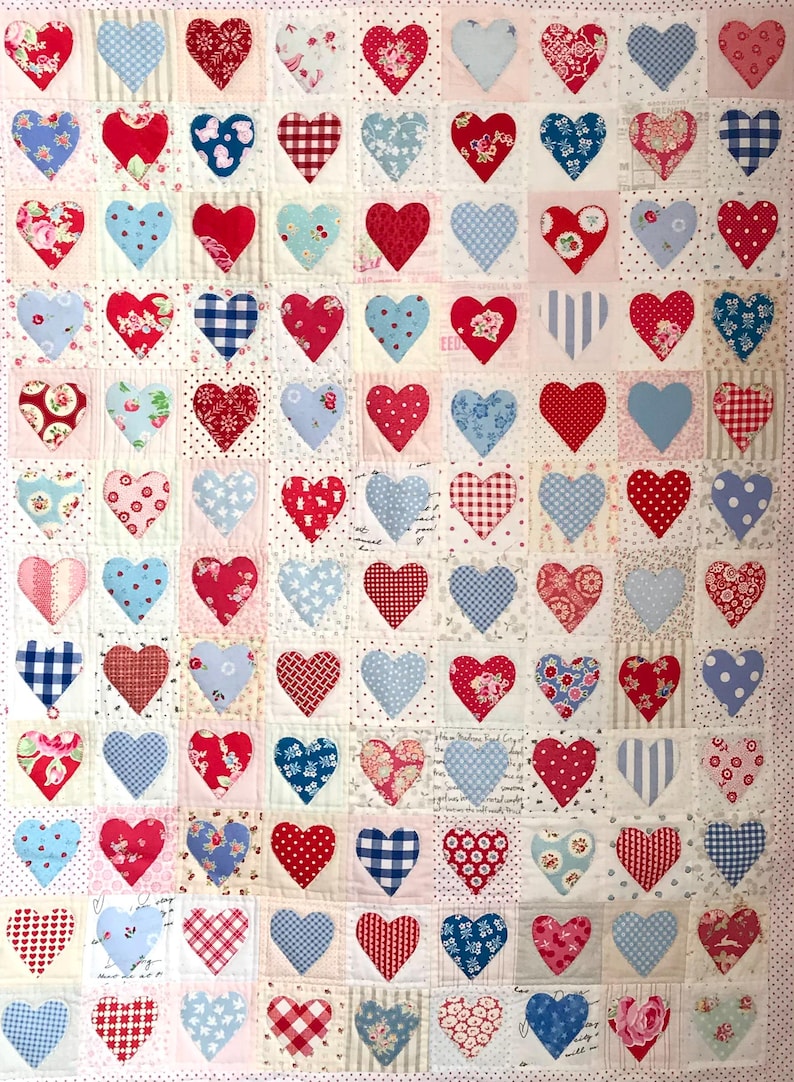 May include: A quilt made of patchwork squares with a heart design in each square. The hearts are in shades of red and blue and are made of different fabrics. The background of the quilt is white with a subtle pattern.