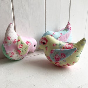 Op de afbeelding: Drie handgemaakte stoffen vogels met bloemenpatronen. De vogels zijn roze, geel en blauw met roze, groene en blauwe vleugels.