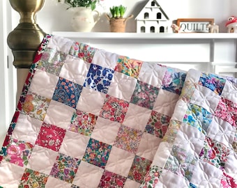 Puede incluir: Una colcha de retazos rosa y blanca con un patrón floral. La colcha está hecha de cuadrados de diferentes telas, cada uno con un diseño floral único. La colcha está doblada y drapeada sobre un cabecero de cama.