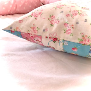 May include: A white pillow with a floral pattern in pink and blue. The pillow is made of patchwork fabric with different floral designs.