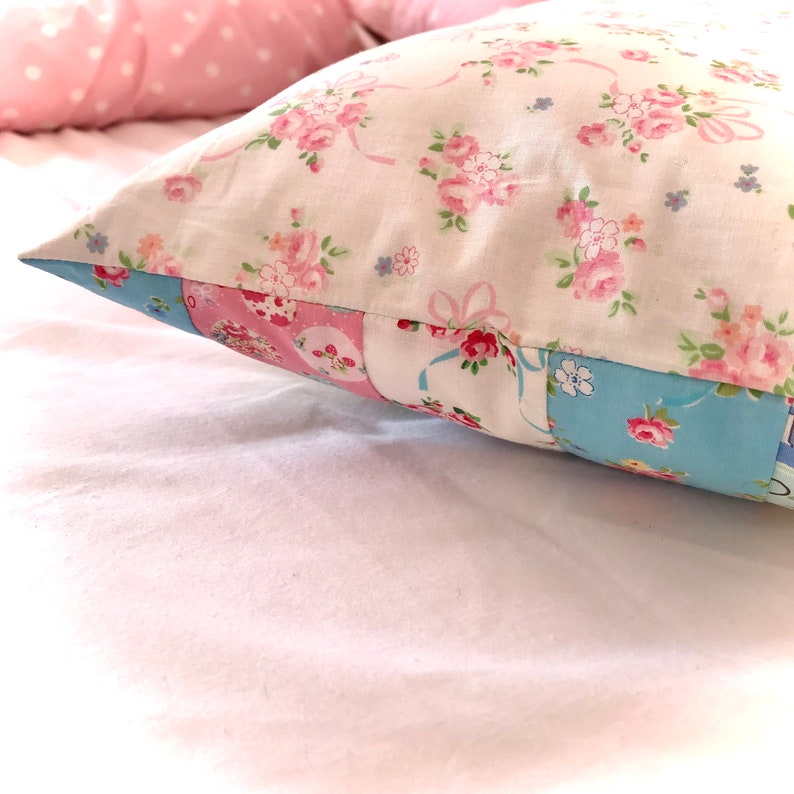 May include: A white pillow with a floral pattern in pink and blue. The pillow is made of patchwork fabric with different floral designs.