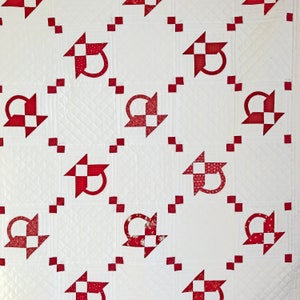 May include: White quilt with a red and white patchwork design. The quilt features a repeating pattern of small squares and a larger square with a red and white basket design.