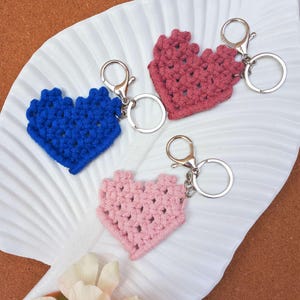 May include: Three crocheted heart-shaped keychains with silver key rings. The keychains are pink, blue, and a darker shade of pink.