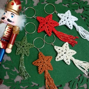 Può includere: Cinque portachiavi a forma di stella con nappine. Le stelle sono fatte di corda annodata in rosso, bianco, verde, marrone e crema. I portachiavi sono attaccati a anelli portachiavi argentati.