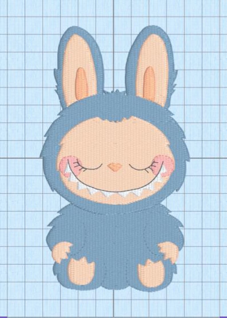 May include: An embroidered design of a friendly monster-bunny hybrid. The creature has light blue fur, large ears, and a peach-coloured face and paws. It has closed eyes, a small nose, and a wide, toothy grin. The design is on a light blue grid background.