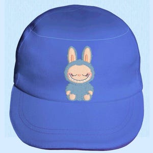 May include: A blue baseball cap with an embroidered cartoon bunny design. The bunny is light blue with pink ears and a smiling face. The cap has a curved peak and a rounded crown, suitable for various head sizes.