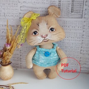 May include: A handmade plush toy mouse with a yellow bow, blue and white striped shirt, and a blue button. The mouse is standing on a white surface with a vase of dried flowers and a sheet of music in the background. The text "PDF Tutorial" is written in red on a white circle.