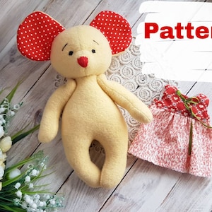 May include: A yellow felt mouse toy with red polka dot ears and a red nose. The mouse is wearing a red and white dress with a green ribbon.