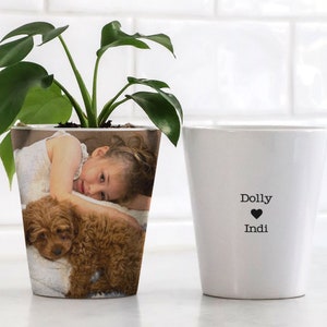 Puede incluir: Maceta de cerámica blanca con una foto de una niña y un cachorro impresa en la parte delantera. El texto "Dolly ♥ Indi" está impreso en la maceta.