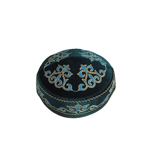 Op de afbeelding: Een donkergroene fluwelen schedelkap met ingewikkeld borduurwerk in felblauw en goudkleurig draad. Het ontwerp bevat symmetrische, bloemachtige patronen op de bovenkant en een doorlopende decoratieve rand langs de onderkant van de kap.