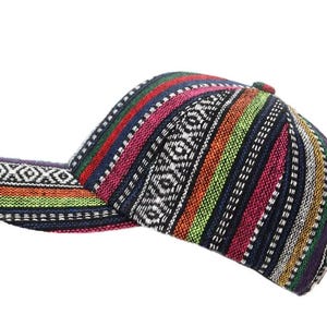 Puede incluir: Una gorra de béisbol con un vibrante patrón tejido multicolor con rayas verticales en tonos rojo, verde, azul, amarillo y morado, acentuado por bandas horizontales de formas geométricas de diamantes en blanco y negro en la visera.