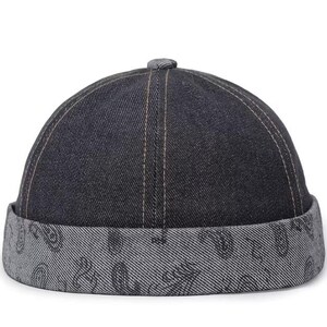 Op de afbeelding: Een donkerblauwe denim docker-pet met een opgerolde rand voorzien van een lichtgrijs paisley-patroon. De kroon is opgebouwd uit zes panelen van donker indigo denim met zichtbare stiksels, wat zorgt voor een gestructureerd ontwerp zonder klep.