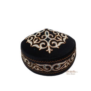 Puede incluir: Un casquete negro con intrincados patrones bordados en blanco y dorado en la parte superior y a lo largo de la banda lateral. El bordado consiste en motivos entrelazados y en espiral que contrastan con la tela oscura del gorro.