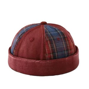 May include: A brimless docker cap featuring a combination of solid dark red panels and blue and red plaid patterned panels. The hat has a thick, rolled-up cuff in a matching dark red fabric and a small button at the top center of the crown.