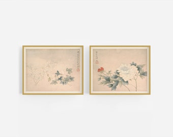 May include: Two framed prints of traditional Japanese floral paintings. The left print features a white flower with green leaves on a light beige background. The right print features a white flower with red accents and green leaves on a light beige background. Both prints have a gold frame.