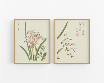 Op de afbeelding: Twee ingelijste prints van Japanse botanische illustraties. De linker print toont een cluster van witte bloemen met roze accenten en groene bladeren. De rechter print toont een wijnstok met kleine gele bloemen en groene bladeren. Beide prints hebben Japanse tekst.