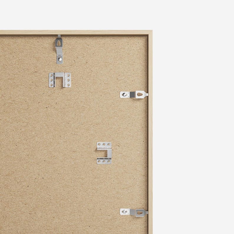 May include: The back of a light brown picture frame with metal hanging hardware attached. The frame is made of wood and has a textured surface.