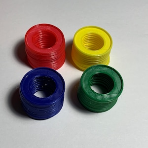 Puede incluir: Cuatro pilas de anillos de pl&aacute;stico de colores. Los anillos son rojos, amarillos, verdes y azules. Cada pila mide aproximadamente 5 cm de alto.