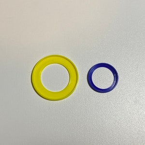 Puede incluir: Dos anillos de pl&aacute;stico, uno amarillo y otro azul. El anillo amarillo es m&aacute;s grande que el anillo azul.