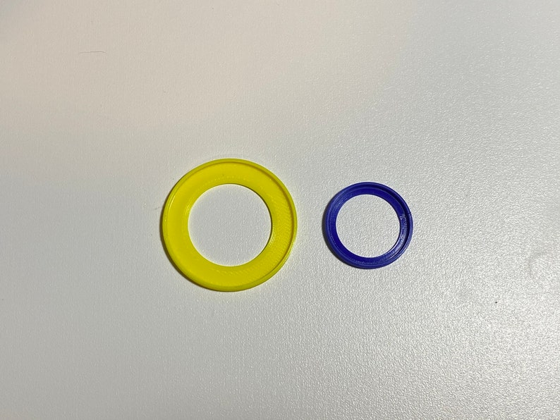 Puede incluir: Dos anillos de pl&aacute;stico, uno amarillo y otro azul. El anillo amarillo es m&aacute;s grande que el anillo azul.