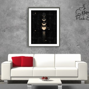 Puede incluir: Una impresi&oacute;n enmarcada de un dise&ntilde;o de fases lunares doradas sobre un fondo negro con estrellas. La impresi&oacute;n est&aacute; colgada en una pared de hormig&oacute;n gris sobre un sof&aacute; blanco con almohadas rojas.