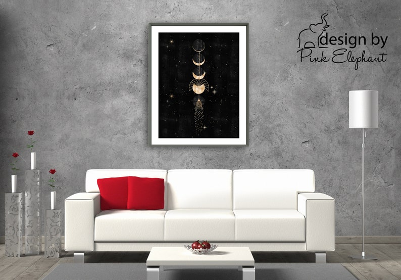 Puede incluir: Una impresi&oacute;n enmarcada de un dise&ntilde;o de fases lunares doradas sobre un fondo negro con estrellas. La impresi&oacute;n est&aacute; colgada en una pared de hormig&oacute;n gris sobre un sof&aacute; blanco con almohadas rojas.