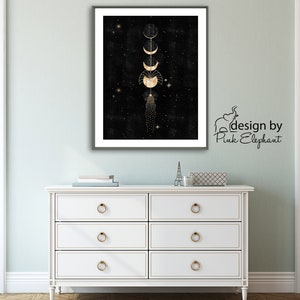 Puede incluir: Una impresi&oacute;n enmarcada en negro y dorado con un dise&ntilde;o de fases lunares doradas sobre un fondo negro con estrellas doradas. La impresi&oacute;n est&aacute; colgada en una pared verde claro sobre una c&oacute;moda blanca con tiradores de cajones dorados. El texto "design by Pink Elephant" est&aacute; en la esquina inferior derecha de la imagen.