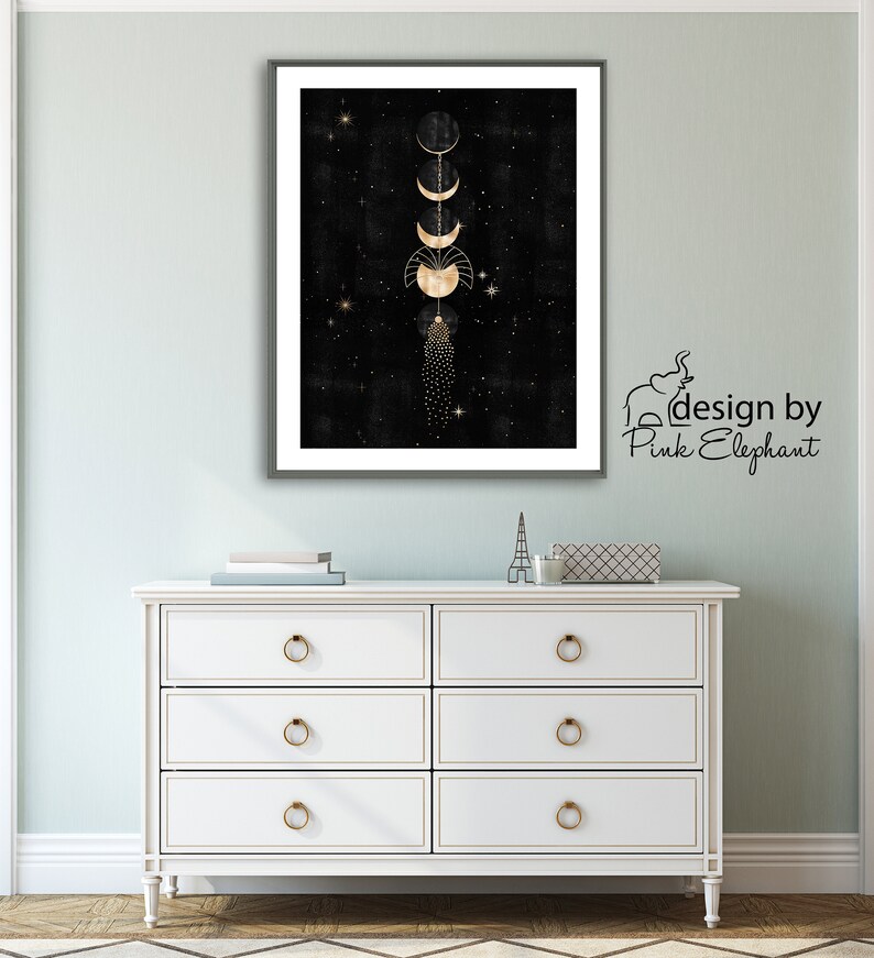 Puede incluir: Una impresi&oacute;n enmarcada en negro y dorado con un dise&ntilde;o de fases lunares doradas sobre un fondo negro con estrellas doradas. La impresi&oacute;n est&aacute; colgada en una pared verde claro sobre una c&oacute;moda blanca con tiradores de cajones dorados. El texto "design by Pink Elephant" est&aacute; en la esquina inferior derecha de la imagen.