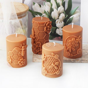 May include: Four brown pillar candles with a honeycomb and bee design. The candles are decorated with raised details of bees, flowers, and honeycomb.