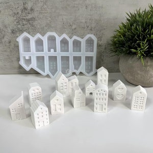 May include: A set of 12 white miniature house moulds, made of silicone, with a variety of designs. The moulds are arranged in a row on a white surface.