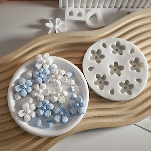 May include: A white silicone mold with six flower shapes and a white plate with blue and white flower-shaped decorations.