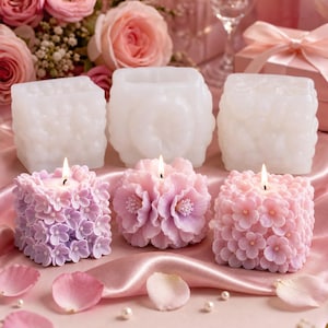May include: An assortment of decorative candles in shades of pink and white. The candles are in the shape of flowers and textured cubes. Lit candles sit on a pink satin surface, with rose petals and flowers in the background.