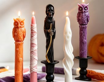 May include: A collection of Halloween-themed candles. The candles include an orange owl, a pink wrapped candle, a black Grim Reaper, a white ghost, and a purple owl. Each candle is lit, and the background includes a pumpkin.