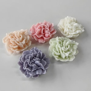 May include: Six decorative flower-shaped items in pastel shades of peach, pink, white, green, and lavender. The flowers have detailed petal designs and are arranged on a white surface. The items appear to be soap or wax.