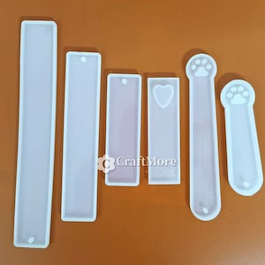 May include: Five white silicone moulds for resin crafts. The moulds are rectangular and feature different designs, including a paw print, a heart, and a plain rectangle.