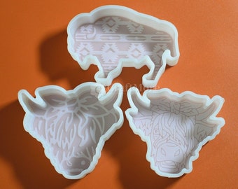 May include: Three white silicone cookie cutters shaped like a buffalo and two cows. The buffalo has a geometric pattern on its body. The cows have detailed facial features and fur.