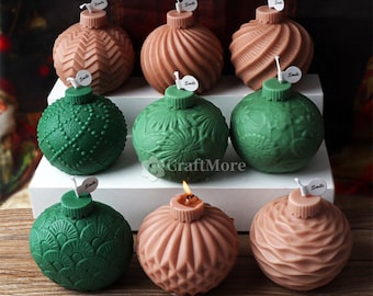 May include: A collection of decorative Christmas ornament-shaped candles in shades of green and peach. Each candle has a unique textured design and a small wick. Some candles have a small tag that says "smile".