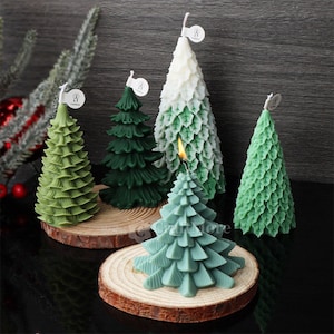 May include: Five green and white Christmas tree candles on wooden bases. The candles are decorated with a leaf pattern and have a white label with the word "Candle" on them.