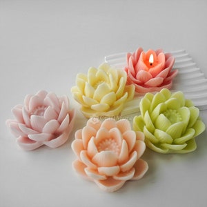 May include: Five lotus flower shaped candles in various pastel colours, including pink, yellow, green, and peach. One candle is lit.