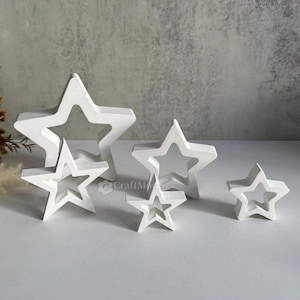 以下が含まれることがあります： 切り抜きデザインの白い木製の星が4つセットになっています。星はサイズが小さくなるように配置されており、一番大きな星が後ろ、一番小さな星が前にあります。