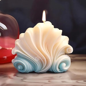 Könnte beinhalten: Eine weiße und blaue Kerze in Form einer Muschel mit einer Flamme oben.