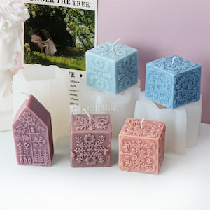May include: Five decorative candles in different shapes and colors. The candles are in the shape of a house, a square, and a cube. The candles are decorated with floral patterns.