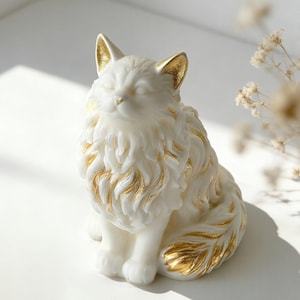 May include: A white cat figurine with gold accents on the ears, fur, and tail. The cat is sitting with its eyes closed, and the fur is detailed with a textured design. The figurine is a decorative item.