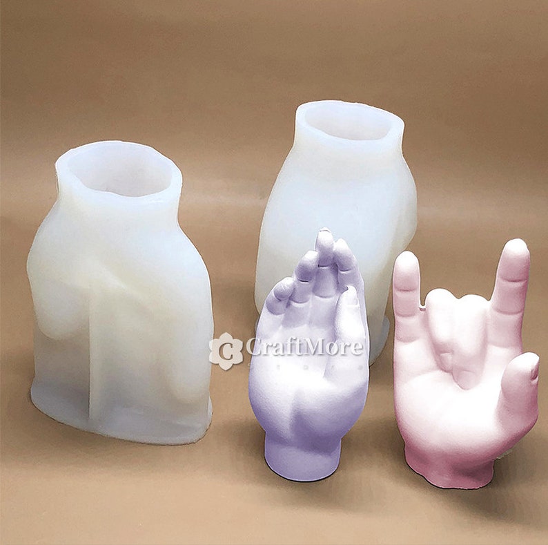 May include: Three silicone molds for making hand-shaped planters. The molds are white and are shown with two finished planters, one in purple and one in pink.