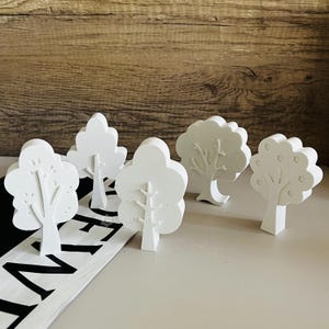 Peut inclure: Cinq figurines d'arbres en bois blanc avec des motifs de branches différents. Les arbres sont posés sur une surface noire et blanche.